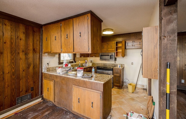 kitchen featuring brown cabinetry, a peninsula, stainless steel microwave, and visible vents