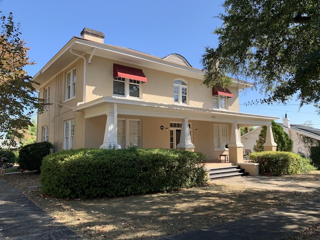 view of front of home with covered porch, a chimney, and stucco siding