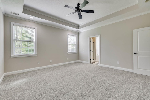 carpeted spare room featuring a raised ceiling, baseboards, ornamental molding, and visible vents