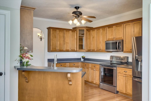 kitchen with a peninsula, ornamental molding, appliances with stainless steel finishes, dark countertops, and light wood finished floors