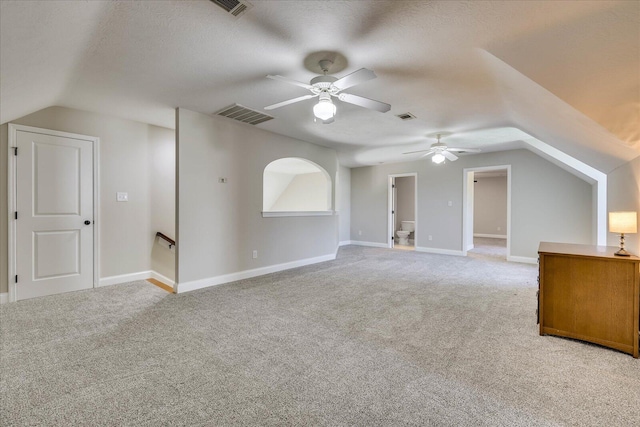 additional living space featuring vaulted ceiling, light carpet, a textured ceiling, visible vents, and ceiling fan