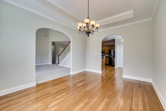 empty room featuring light wood-type flooring, baseboards, a chandelier, a raised ceiling, and arched walkways
