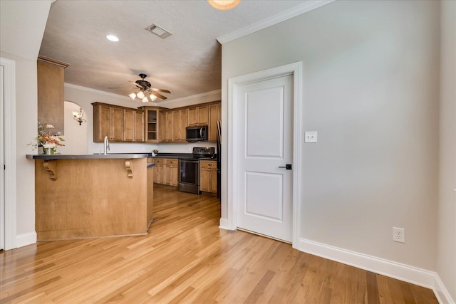 kitchen with a kitchen bar, a peninsula, visible vents, stainless steel appliances, and brown cabinets