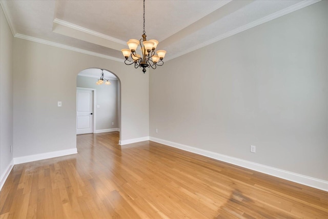 spare room featuring baseboards, arched walkways, an inviting chandelier, light wood-style floors, and a tray ceiling
