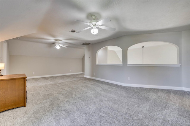 spare room with baseboards, vaulted ceiling, light carpet, a ceiling fan, and visible vents