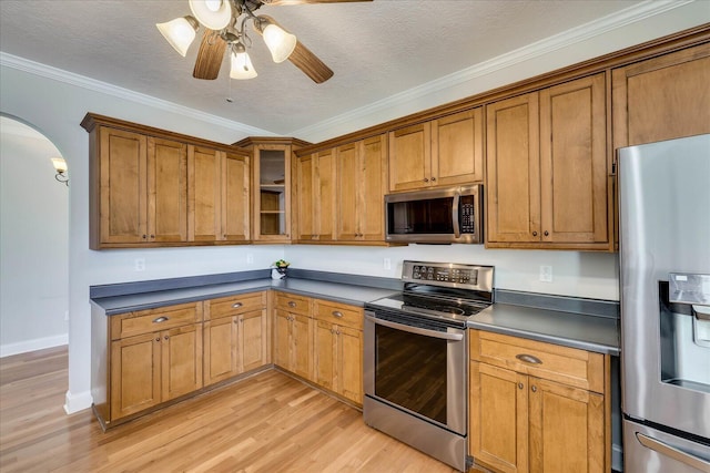 kitchen with stainless steel appliances, arched walkways, light wood finished floors, and dark countertops