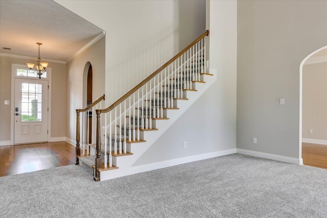 carpeted foyer entrance featuring arched walkways, baseboards, ornamental molding, and stairs