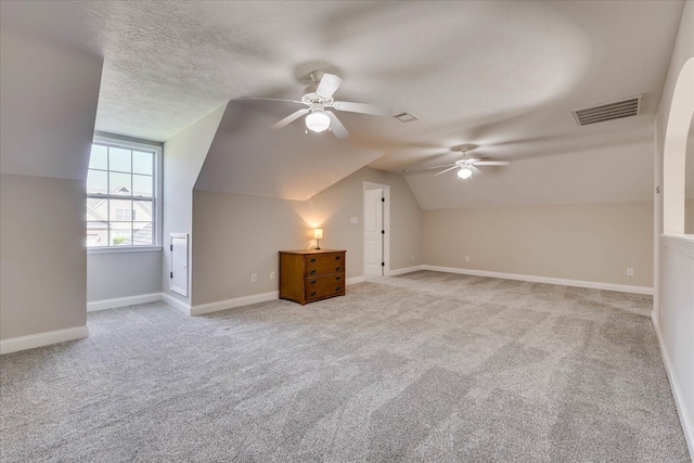 additional living space featuring a textured ceiling, carpet flooring, a ceiling fan, and visible vents