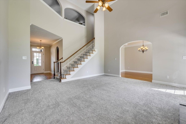unfurnished living room with ceiling fan with notable chandelier, a towering ceiling, visible vents, carpet flooring, and stairs