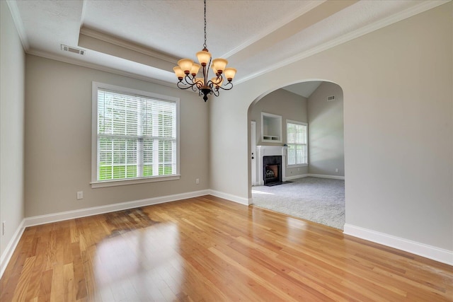 spare room featuring visible vents, a tray ceiling, arched walkways, and light wood-style floors