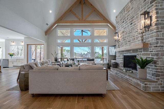 living room featuring high vaulted ceiling, a fireplace, and light hardwood / wood-style floors