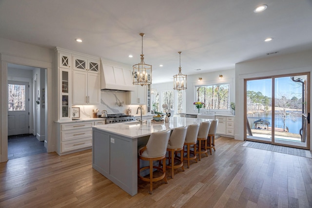 kitchen with white cabinetry, pendant lighting, custom range hood, and a center island with sink