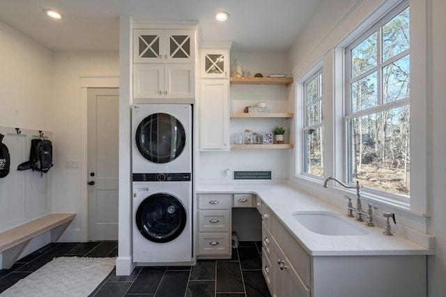 clothes washing area with stacked washer and dryer, sink, and cabinets