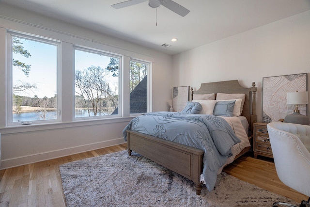 bedroom with light hardwood / wood-style flooring, ceiling fan, and a water view