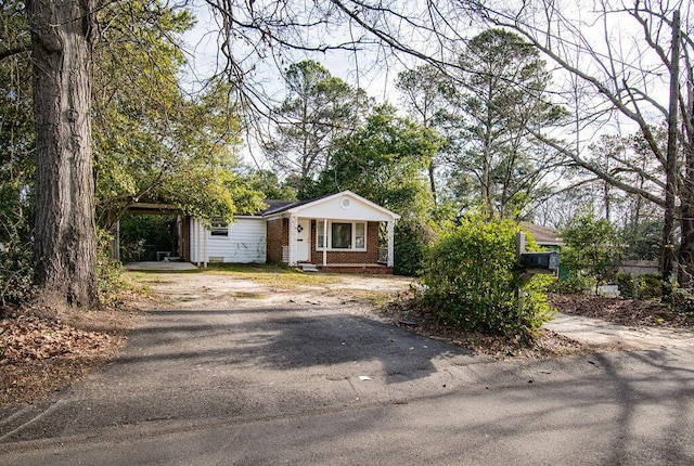 view of front of house with covered porch, driveway, brick siding, and a carport