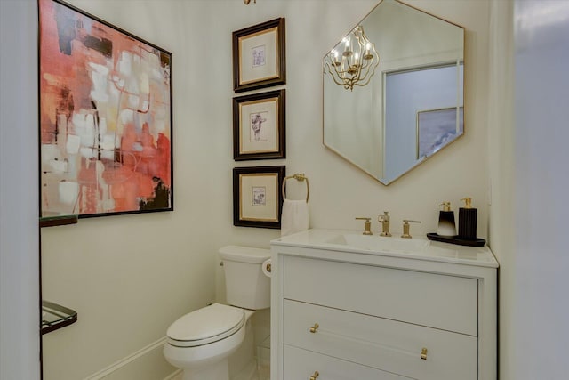 half bathroom featuring baseboards, vanity, toilet, and an inviting chandelier