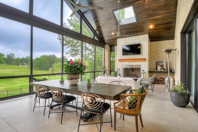 sunroom / solarium featuring ceiling fan, vaulted ceiling with skylight, a fireplace, and wood ceiling