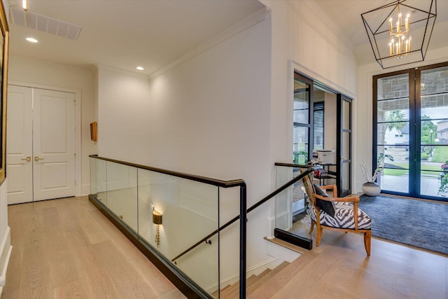 hallway featuring light wood-style floors, visible vents, a notable chandelier, and ornamental molding