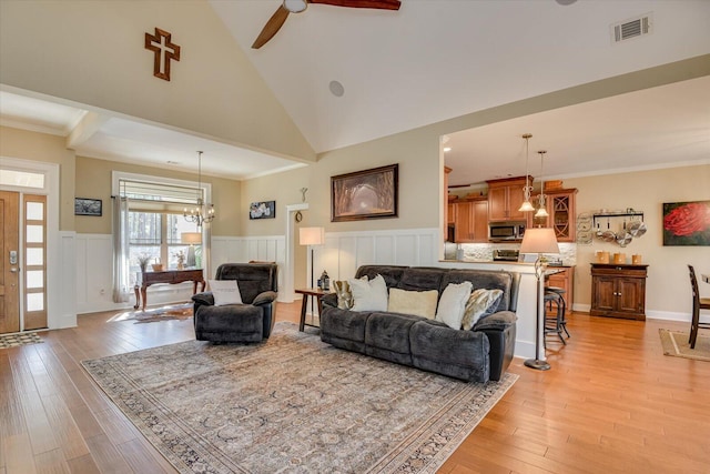 living area with light wood finished floors, visible vents, crown molding, a wainscoted wall, and ceiling fan with notable chandelier