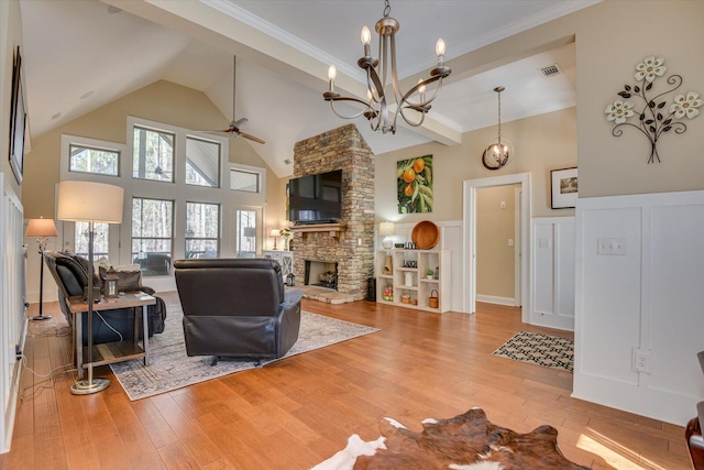 living area featuring a wainscoted wall, visible vents, light wood finished floors, a stone fireplace, and ceiling fan with notable chandelier