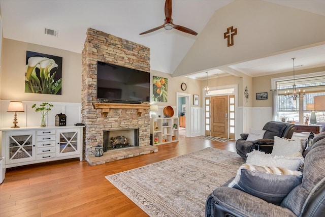 living room with a wainscoted wall, visible vents, high vaulted ceiling, ceiling fan with notable chandelier, and wood finished floors