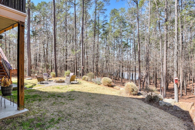 view of yard featuring a view of trees, stairway, a patio area, and an outdoor fire pit