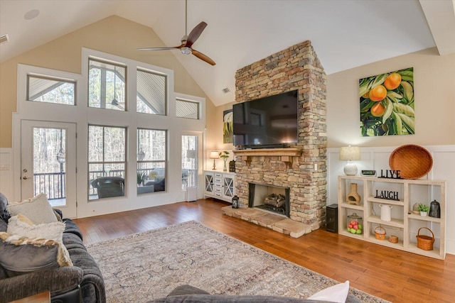 living area with high vaulted ceiling, a stone fireplace, a ceiling fan, and hardwood / wood-style flooring