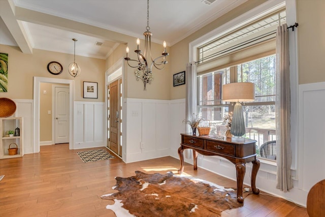 entrance foyer with an inviting chandelier, light wood-style floors, a wainscoted wall, and visible vents