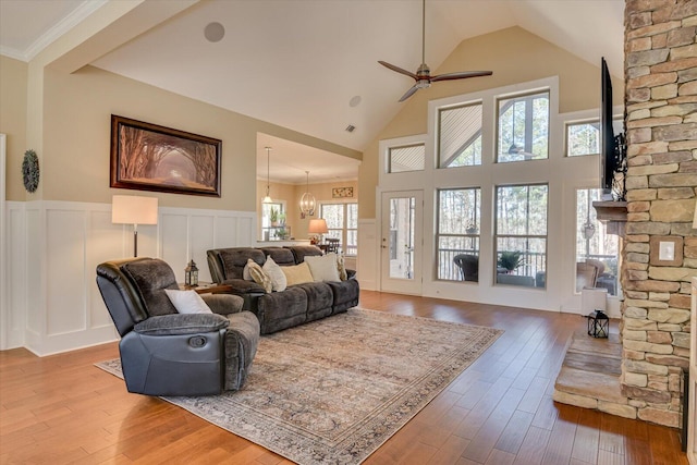 living room with a wainscoted wall, a fireplace, wood finished floors, high vaulted ceiling, and a ceiling fan