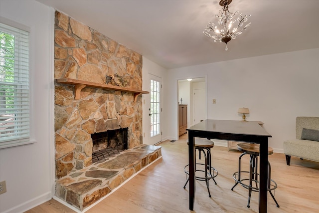 living room with baseboards, light wood-style floors, a stone fireplace, and a chandelier