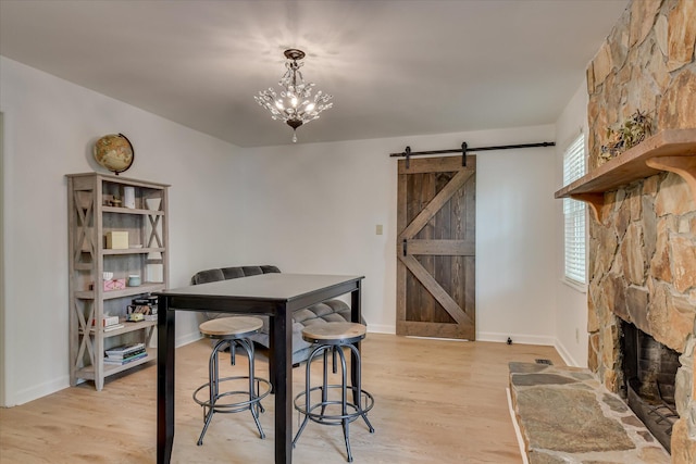 dining area with a barn door, light wood-style floors, a stone fireplace, baseboards, and a chandelier