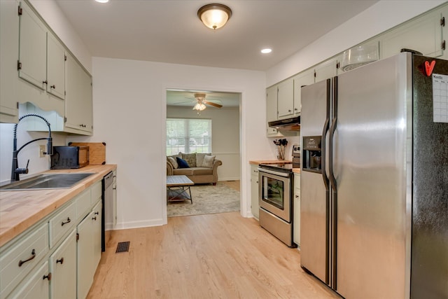 kitchen featuring appliances with stainless steel finishes, a sink, light wood-style flooring, under cabinet range hood, and baseboards