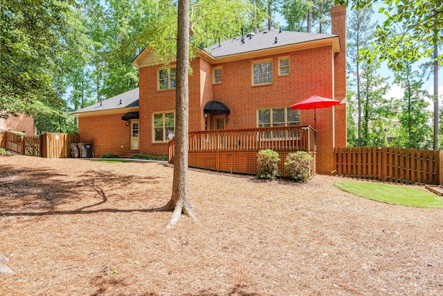 rear view of property with a chimney, fence, brick siding, a deck, and a shingled roof