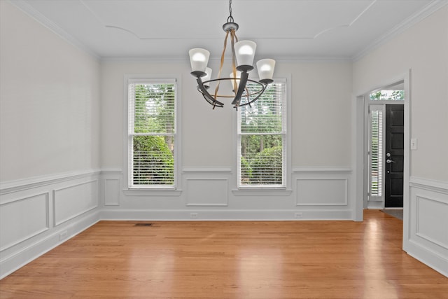unfurnished dining area with a chandelier, light wood-style flooring, a wainscoted wall, and crown molding
