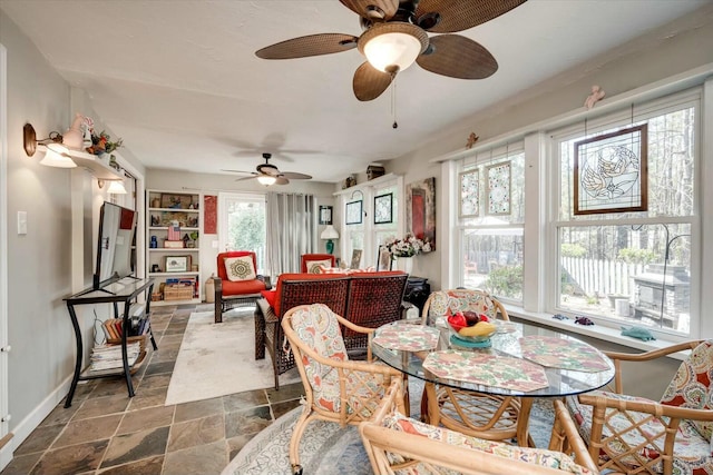 dining area featuring baseboards, a ceiling fan, and stone finish floor