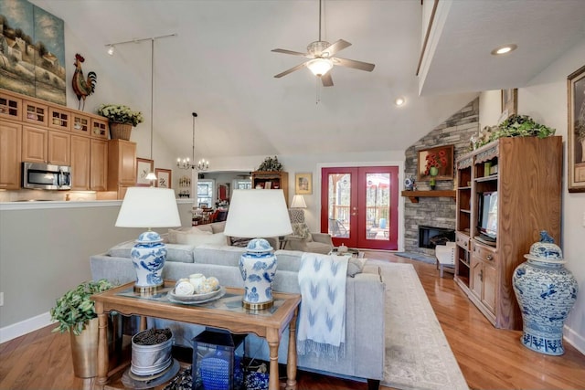 living area with high vaulted ceiling, a stone fireplace, light wood-style flooring, and ceiling fan with notable chandelier