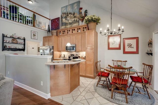 kitchen featuring a notable chandelier, a breakfast bar, light brown cabinets, appliances with stainless steel finishes, and glass insert cabinets