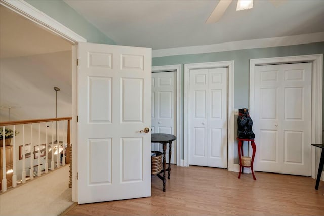 bedroom featuring light wood-style flooring, a ceiling fan, and two closets