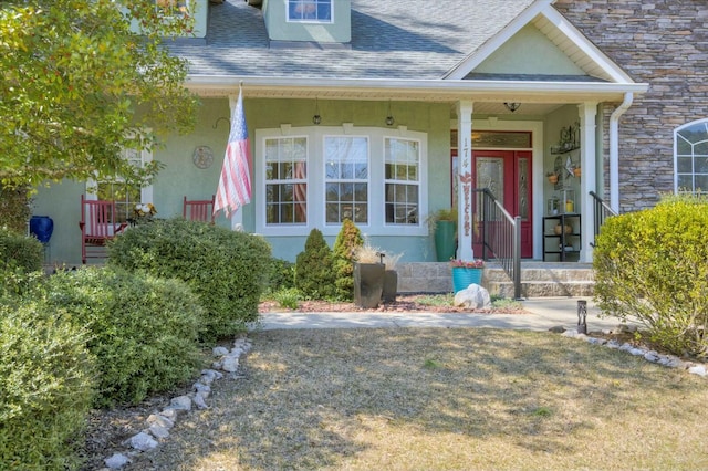 doorway to property featuring covered porch, stone siding, roof with shingles, and stucco siding