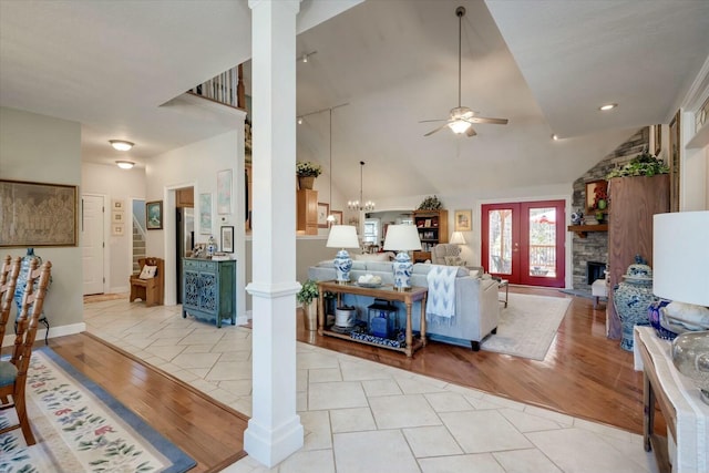 living area featuring high vaulted ceiling, a ceiling fan, a stone fireplace, light wood finished floors, and decorative columns