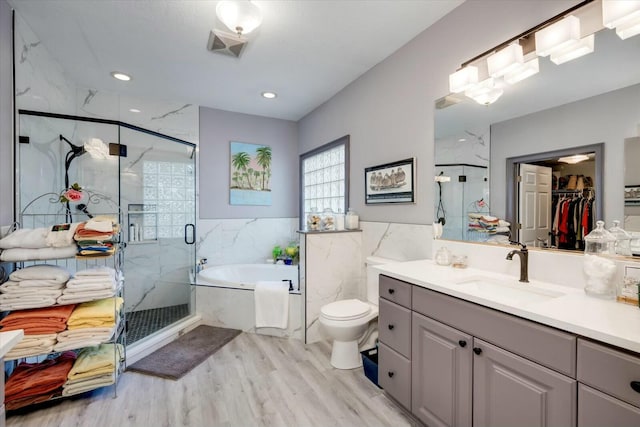 bathroom with a walk in closet, a garden tub, wood finished floors, a marble finish shower, and vanity