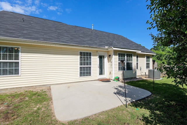 back of house featuring central AC unit, roof with shingles, a patio, and a lawn