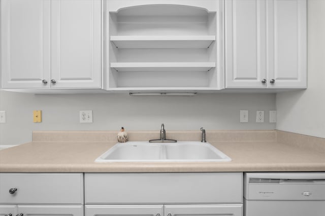 kitchen featuring white dishwasher, light countertops, white cabinets, and a sink