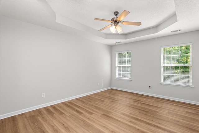 empty room featuring a raised ceiling, a wealth of natural light, light wood-type flooring, and visible vents