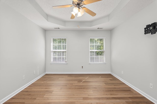 empty room with wood finished floors, a textured ceiling, visible vents, a ceiling fan, and a tray ceiling
