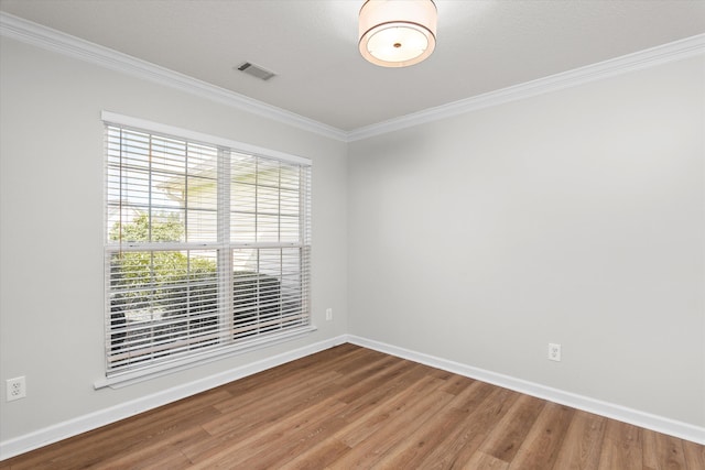 empty room with ornamental molding, baseboards, visible vents, and wood finished floors