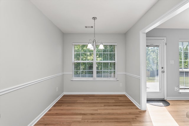 unfurnished dining area featuring an inviting chandelier, baseboards, visible vents, and wood finished floors
