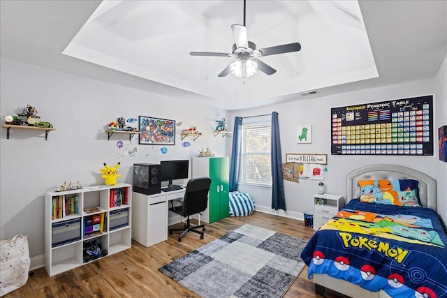 bedroom with hardwood / wood-style flooring, ceiling fan, and a tray ceiling