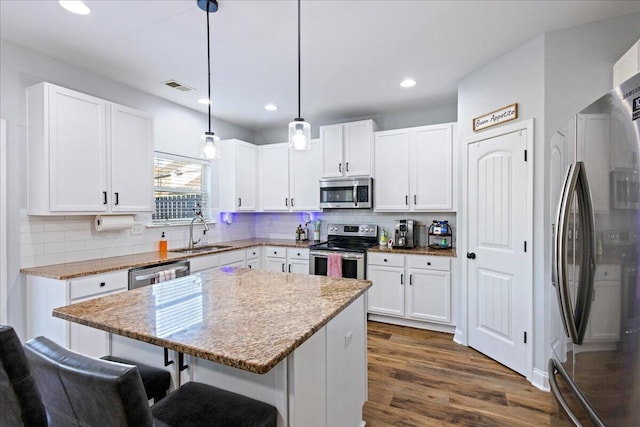 kitchen featuring tasteful backsplash, stainless steel appliances, decorative light fixtures, white cabinets, and a center island