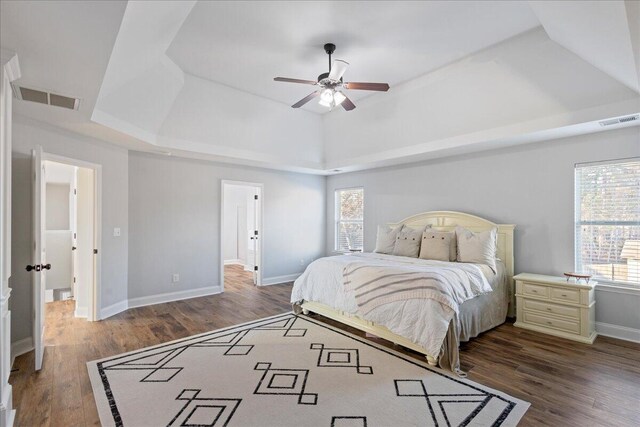 bedroom with multiple windows, dark hardwood / wood-style floors, a raised ceiling, and ceiling fan